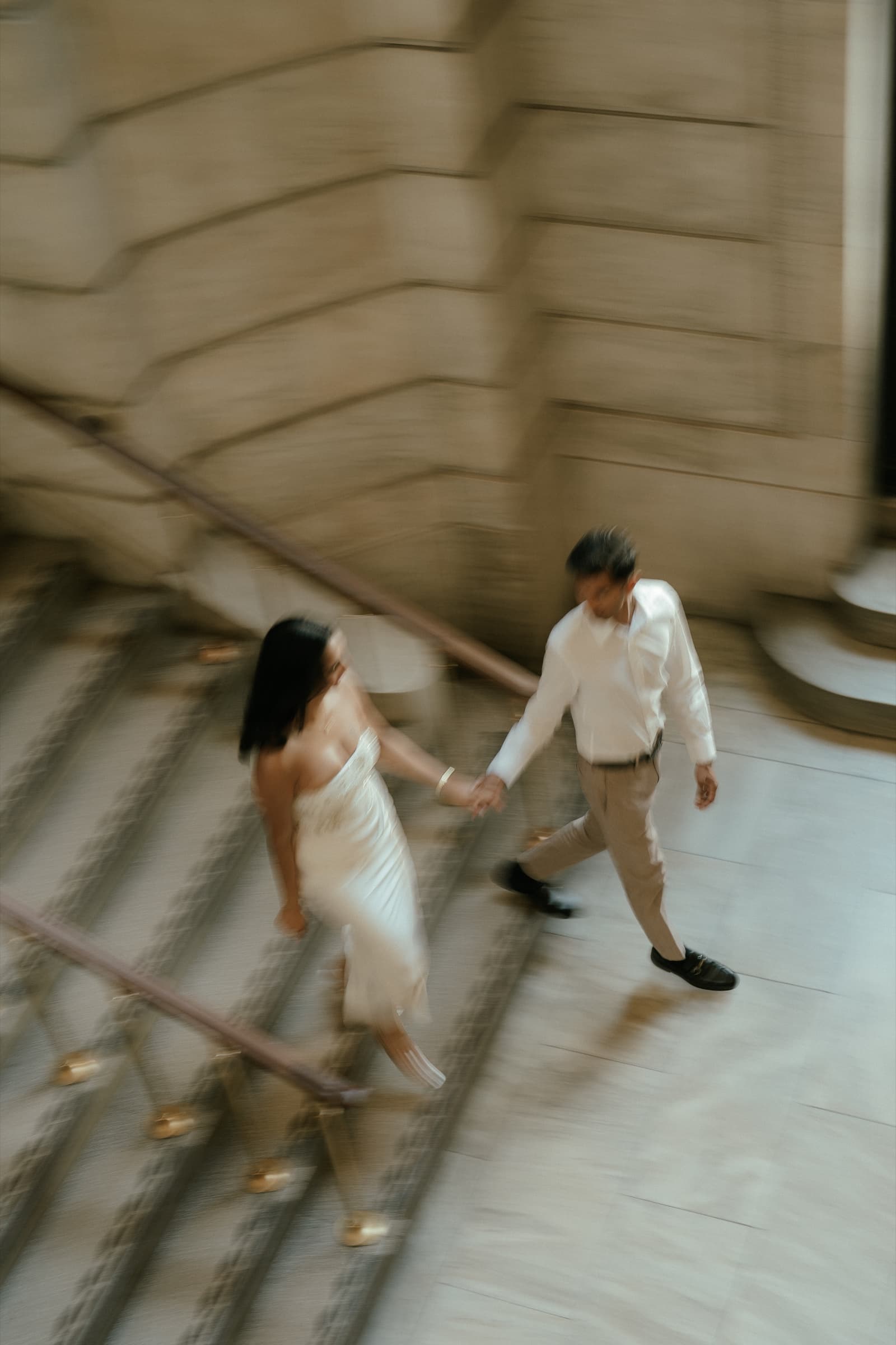 Motion-blurred overhead view of Ananya and Varun holding hands on a marble staircase